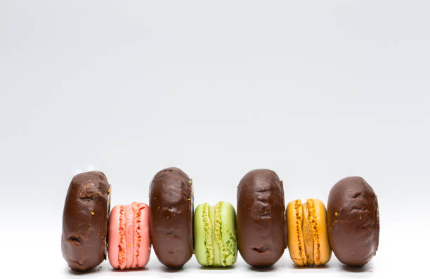 istock Colored donuts and macaroons placed alternately on white background.  French cookies. Sweets with sugar.  Colored buns and macarons. 1413086516