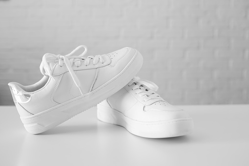 White women's leather sneakers on white background top view flat lay. Stylish youth sneakers, sports shoes, genuine leather footwear. Minimalistic shoe store advertising fashion style Shoe background