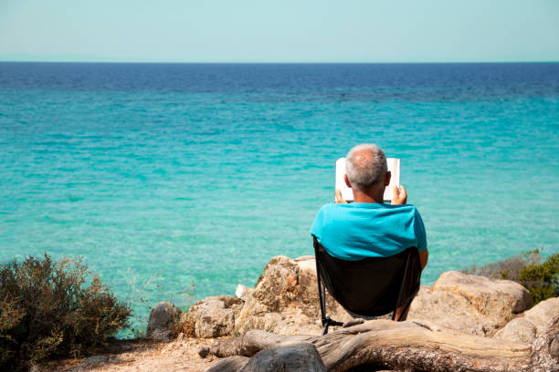 Man is reading a book next to the see