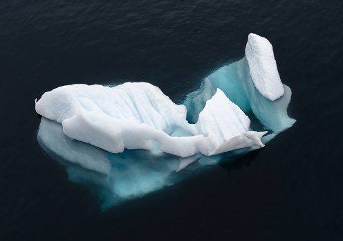 From above a small iceberg shows its delicate shape both above and below the surface of the sea. Dark background gives drama to the form and isolates its interest. Taken in Neko Harbor of the Antarctic Peninsula.