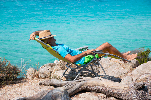 Portrait of a handsome man lying on a deckchair and resting. Happy mature man next to  the beach on Aegean sea. Summer vacation concept.