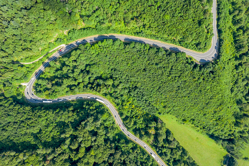 Aerial view of windy road in middle of forest, beautiful lush trees, curvy holiday road trip.