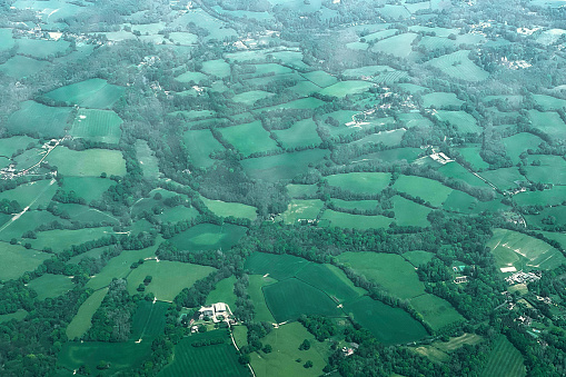 Agricultural fields and farm buildings with green areas surrounded by trees and country roads, as seen from an airplane flying over Britain's countryside.
