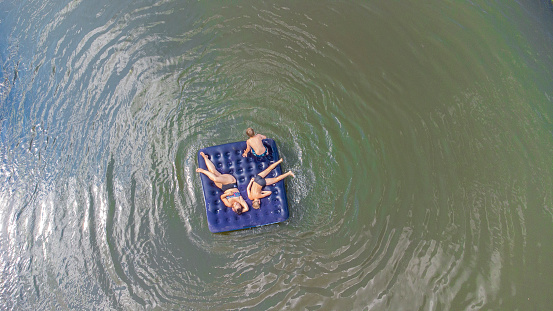 Happy kids with mom float on an inflatable mattress on the river