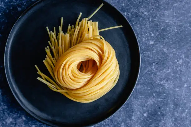 Overhead view of a fresh uncooked spaghetti pasta nest on a dark ceramic plate