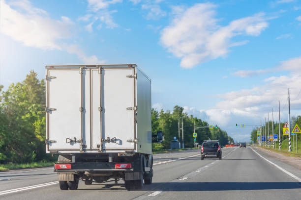 晴れた日に高速道路を走る軽トラック。白い近代的な配達小型貨物宅配便トラックは、都市郊外への高速道路道路を高速で移動します。ビジネス物流エクスプレスサービス。 - car delivering white mini van ストックフォトと画像