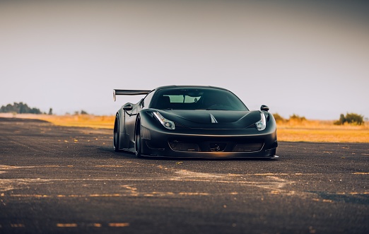 LA, CA, USA April 4, 2022 Ferrari 458 widebody in black driving on the road with trees on both sides of the road