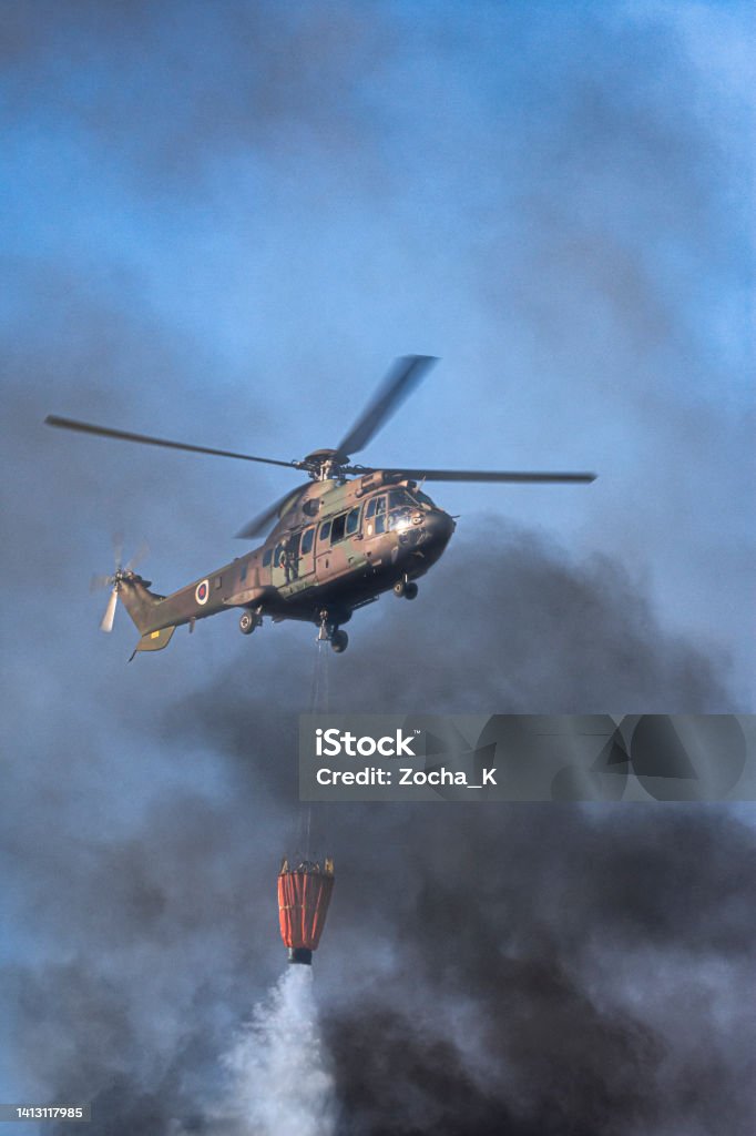 Military helicopter assists firefighters in extinguishing forest fire Close-up of a military helicopter assists firefighters in extinguishing a forest fire. A helicopter is dropping water, shrouded in smoke. Air Vehicle Stock Photo