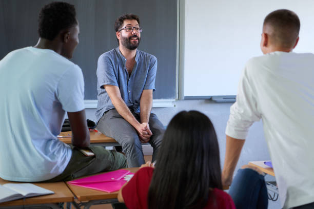istock Teacher involved with students at college sitting on his desk while giving an interactive class. 1413119699