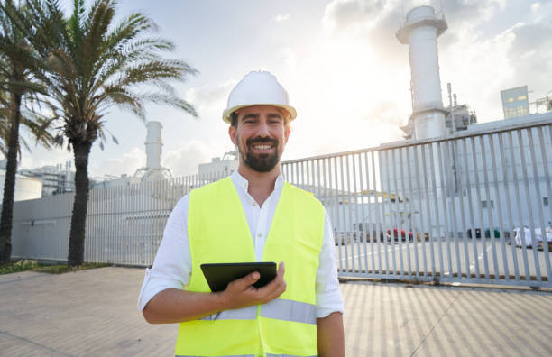 istock Cheerful young engineer man looking at camera, holding a digital tablet while standing outside an electrical plant. Concept, renewable energy generation. 1413122584