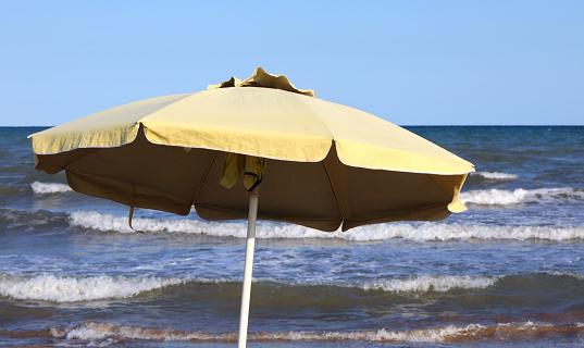 Yellow umbrella to protect yourself from the sun on the seashore moved by the waves in the summer