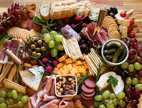 A delicious array of cheeses, charcuteries, fruit, breads and fancy crackers all on a board for sharing while entertaining friends for an evening.