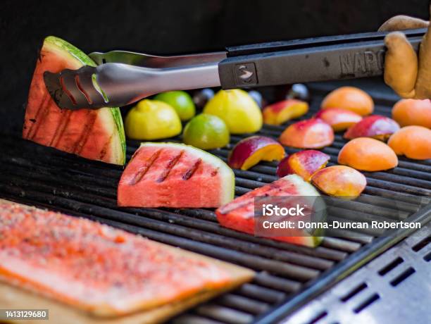 A Summer Barbecue Cooking Up Grilled Fruit And Salmon Fillet On A Plank For A Fresh Meal Stock Photo - Download Image Now