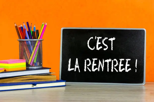 Back to school concept - blackboard with french word : c'est la rentrée with pencil-box and books, notebook and sticky note on wooden table