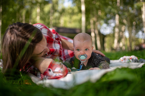 Mother with a child are lying on a plaid on the grass at a campsite in the forest