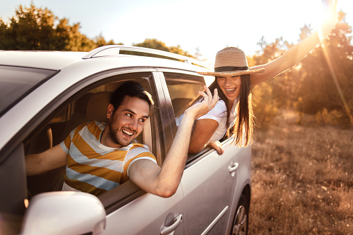 Young beautiful couple having fun while riding a car in nature