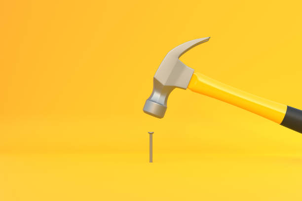 istock Hammer with a steel head and a yellow plastic handle banging a small screw on yellow background 1413138229