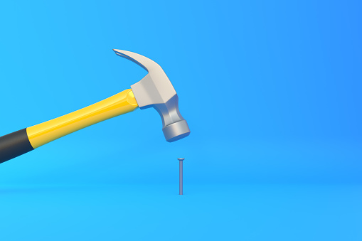Hammer with a steel head and a yellow plastic handle banging a small screw on blue background. Front view, minimalism. Copy space. 3d rendering illustration