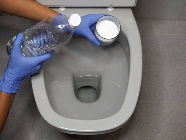 las manos femeninas con guantes sostienen un vaso de bicarbonato de sodio y una botella de vinagre blanco sobre la taza del inodoro - water bottle water bottle drink fotografías e imágenes de stock