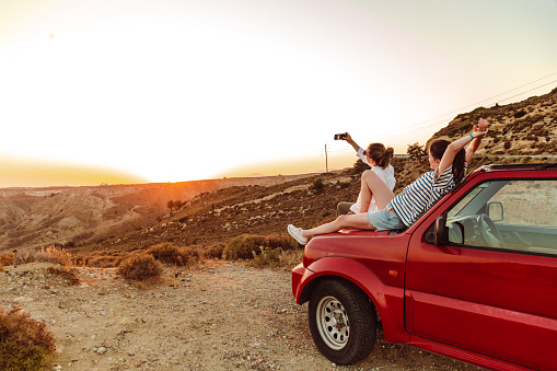 Two cheerful young women enjoying a summer’s road trip. They are looking at the view and enjoying the sunset