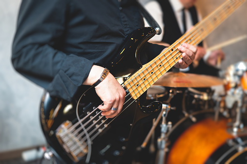 Concert view of musician, electric bass guitar player with during band performing rock music,  bassist player on stage