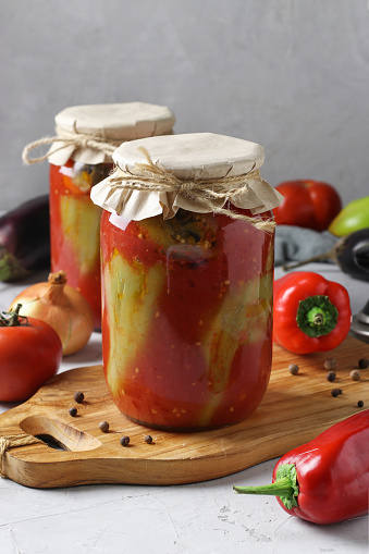 Peppers stuffed with eggplant and onions, in tomato sauce, in two glass jars on gray background, Vertical format