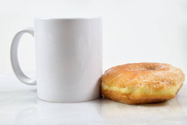 A delicious sugar coated donut sits temptingly next to an 11 oz. coffee cup.