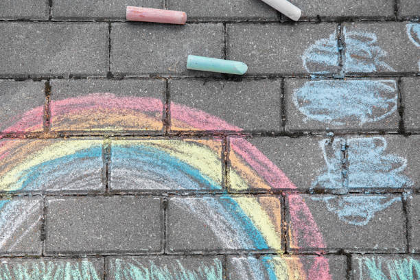 istock Rainbow with grass and clouds painted in colored chalk on a path on the street 1413143378
