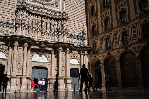 Monistrol de Montserrat, Barcelona-Spain. May 26, 2022: Facade and courtyard at the entrance of the Basilica of the Benedictine Abbey of Montserrat. Tourists and pilgrims visiting to admire the sculpture depicting the Virgin Mary holding the baby Jesus.