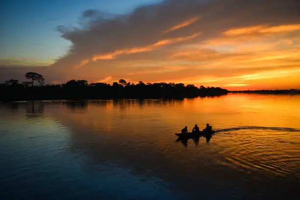 The silhouette of a small motorized canoe on the Guaporé - Itenez river at dusk, Ricardo Franco village, Vale do Guaporé Indigenous Land, Rondonia, Brazil, on the border with Bolivia