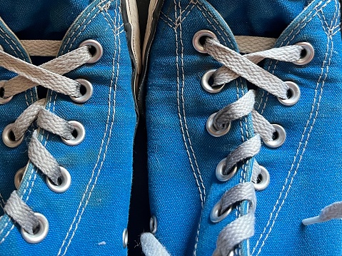 A close-up image of two old blue converse-like sneakers laced up. The sneakers are clearly well-used and scuffed with grass stains.