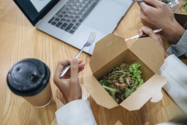 istock Business people eating breakfast and meeting at table in open plan office 1413155768