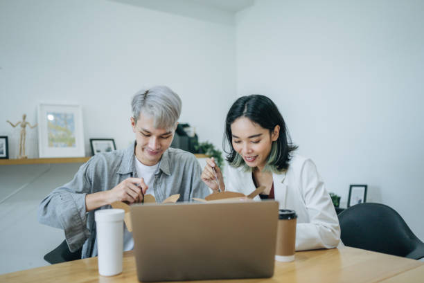 istock Two happy young asian having take out lunch together in office. 1413155775