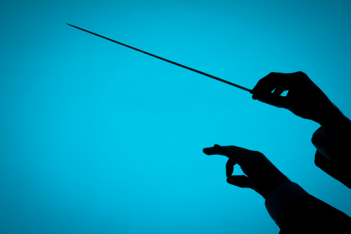 Male orchestra conductor hands, one with baton. Silhouette against blue background.