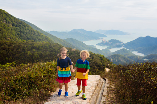 Brothers and sister having fun sightseeing Italian town. The kids are sitting on the rocks and laughing at the camera.\nNikon D850