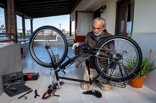 Bicycle maintenance tools, keys. Inverted bicycle. Man in 60 repairing bicycle, feeling young dynamic. Terrace of the house. High vigor, active lifestyle