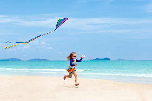 Playful kids playing with a kite, on the beach during their sea vacation