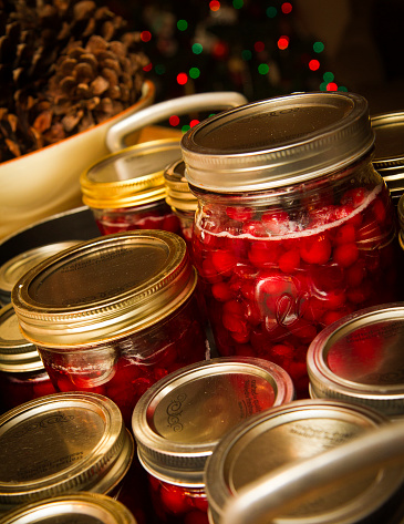 Group of homemade canned cranberries with festive colored lights and pine cones in background