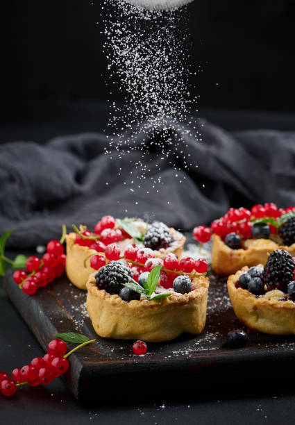istock Fruit tart with red currants sprinkled with powdered sugar on a black table 1413164976