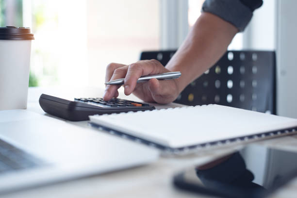 istock Close up man doing finance at home office, using calculator to calculate expenses on notebook with laptop computer, coffee and mobile phone on office table 1413190327