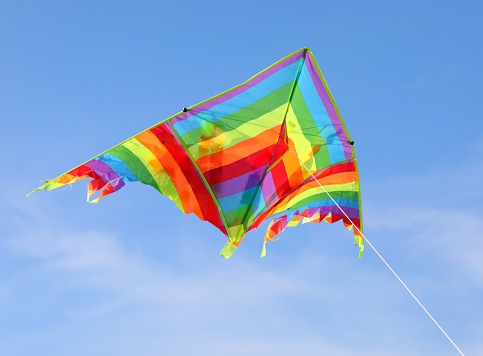 colorful kite with many colors flying high in the blue sky tied to a string