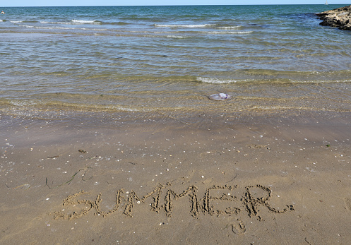 large text with the word SUMMER in capital letters on the sand of the sandy beach by trhe sea