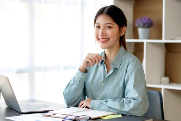 istock Smiling beautiful young Asian businesswoman sitting with laptop and computer while doing some paperwork at the office. Looking at camera. 1413194329