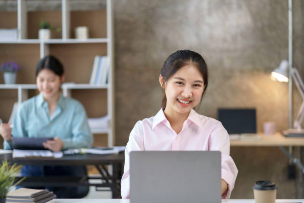 istock Smiling beautiful young Asian businesswoman sitting with laptop and computer while doing some paperwork at the office. Looking at camera. 1413194330