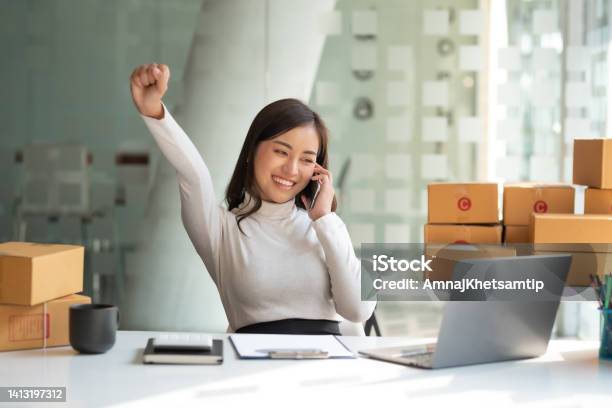 Young Asian Small Business Owner Successful Selling Online And Holding Smartphone With Laptop Computer Happy Asian Business Woman Successful Excited Raised Hands Rejoicing Stock Photo - Download Image Now