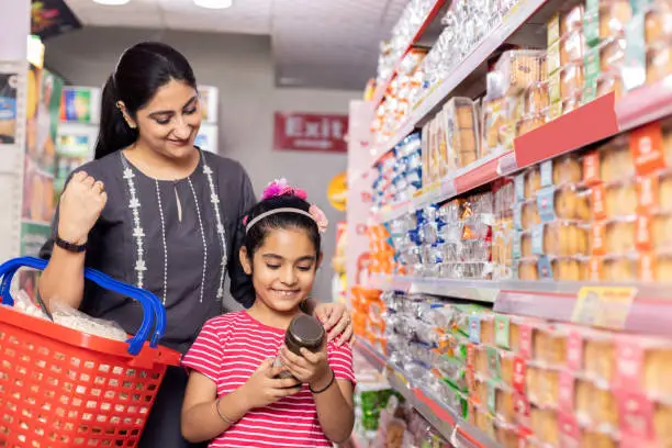 Photo of Happy mother and daughter reading product information while shopping at supermarket