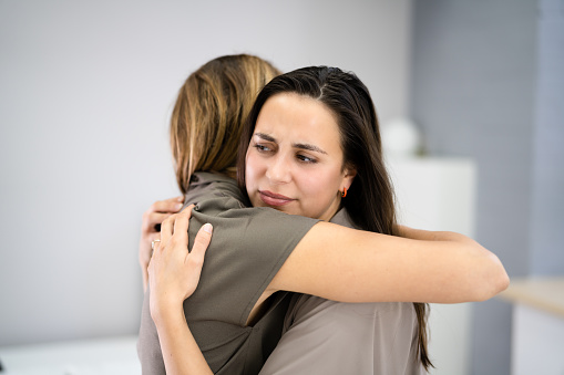 Woman hugging her depressed friend at home, closeup. Young girl supporting her crying girlfriend. Friendship consoling and care, copy space