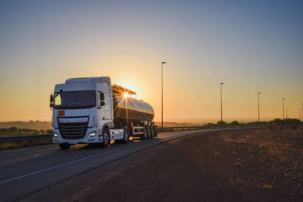 Tanker truck with dangerous goods driving along a lonely road with the sun in backlight Tanker truck with dangerous goods driving on a lonely road fuel tanker stock pictures, royalty-free photos & images