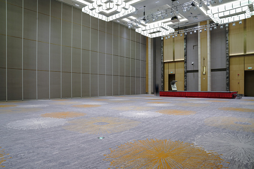 Side view of an empty large warehouse interior with white brick side walls and rough floor illuminated by natural light from ceiling lights and large roof windows. Focus on the side walls. 3D rendered image.