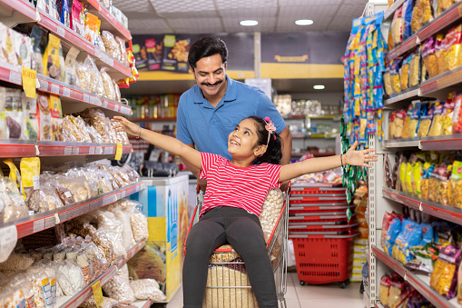 Dad is giving his daughter a ride in the shopping trolley while they're buying food in the supermarket